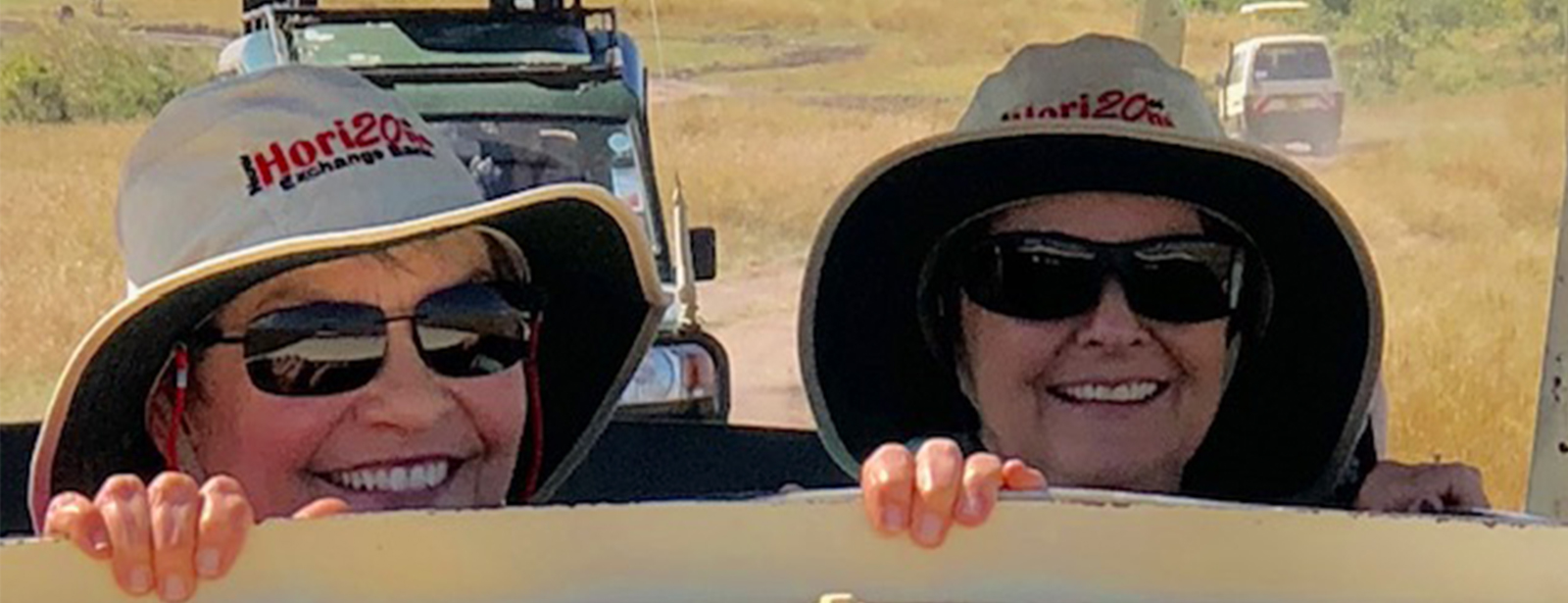 Two women wearing New Horizons hats, smiling and looking out of a safari jeep